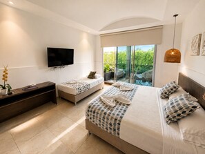 A modern hotel room with a large bed, a smaller bed, a TV, a desk, and a balcony with a view of greenery.