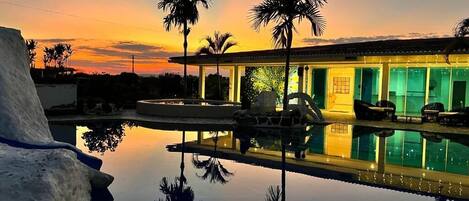 Piscina con el reflejo de palmeras y un edificio con iluminación verde.