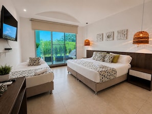 Un dormitorio moderno con dos camas, televisión, escritorio y balcón con vistas a zonas verdes.