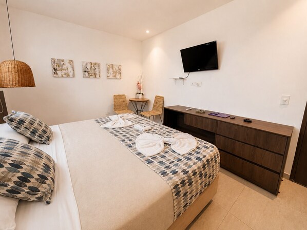 A hotel room with a bed, a desk, a TV, and artwork on the wall.