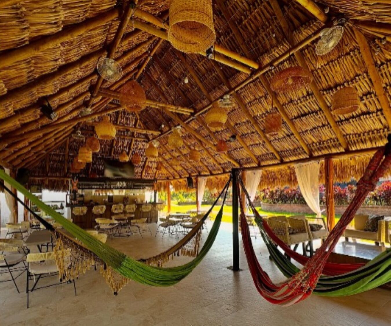Una estructura de techo de paja con hamacas y mesas, que sugiere un espacio informal para sentarse al aire libre.