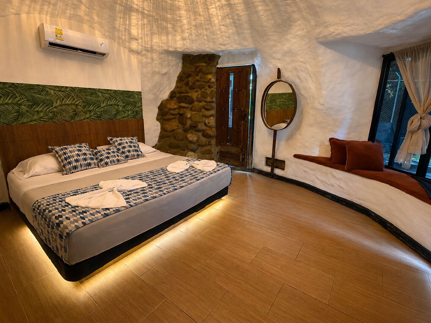 Quarto com cama, parede de pedra, espelho e janela com cortinas.
