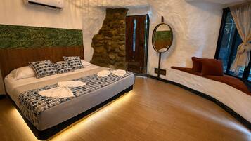Quarto com cama, parede de pedra, espelho e janela com cortinas.