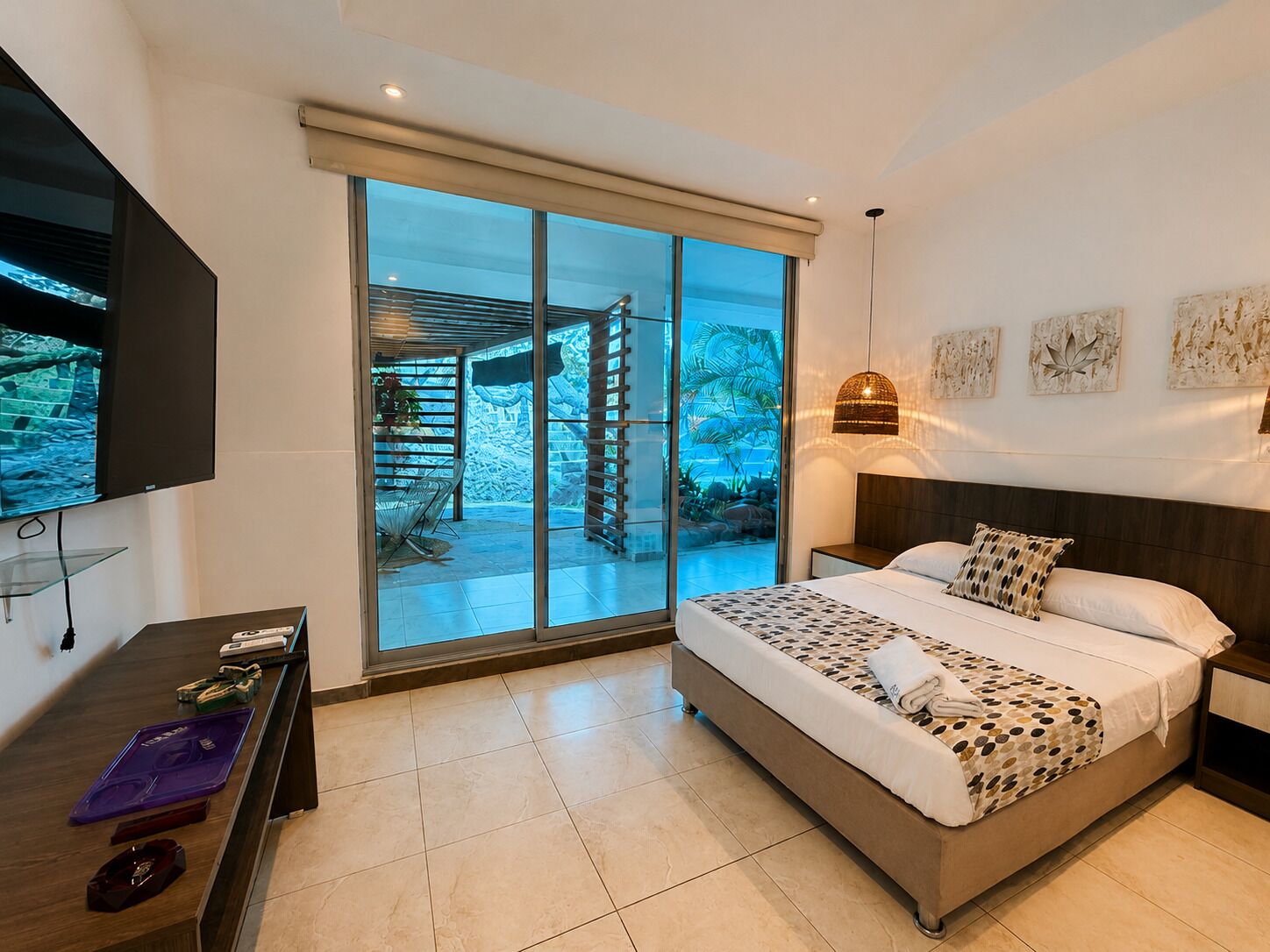 A modern bedroom with a large bed, a television, a desk, and a sliding glass door leading to a balcony.