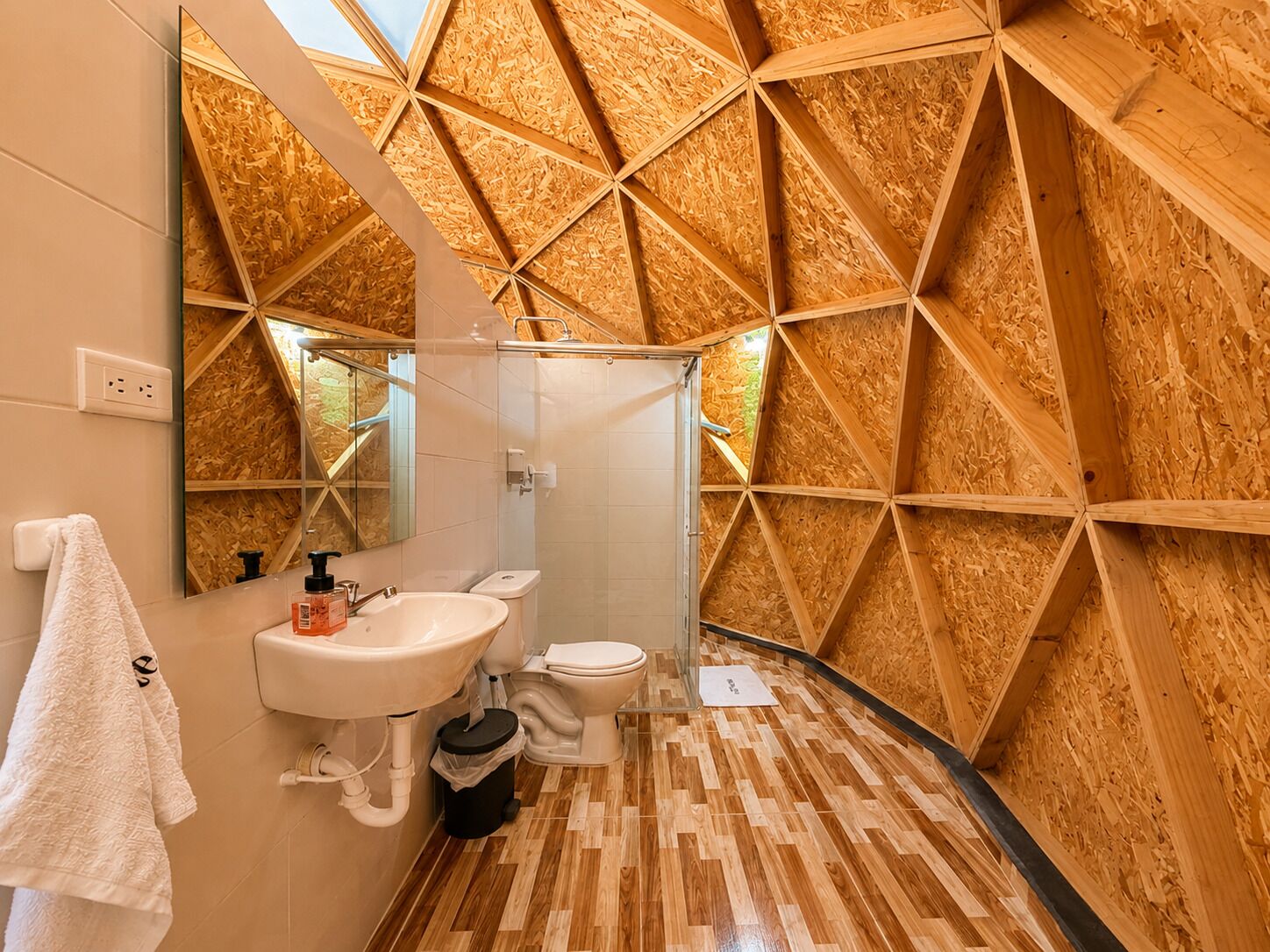 Une salle de bain avec un mur décoré de lambris en bois, un lavabo blanc, des toilettes et un miroir.