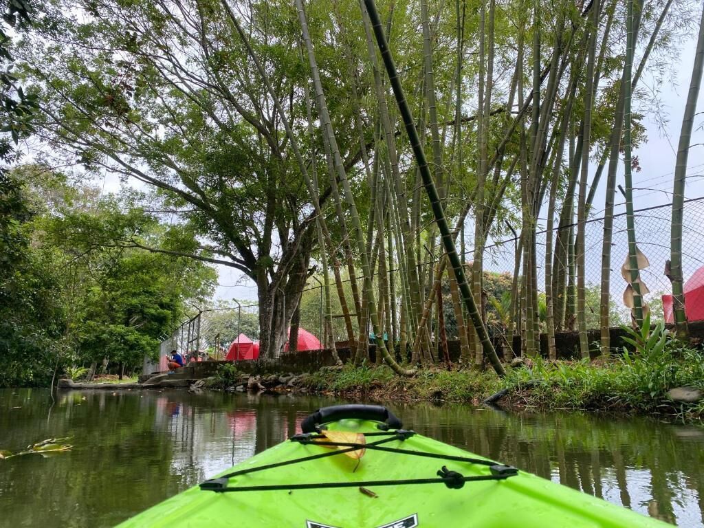 Ein grünes Kajak auf einem ruhigen Fluss, im Hintergrund Bambus und ein rotes Zelt.