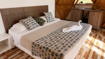 Un dormitorio con cabecera de madera, cama con ropa de cama estampada, toalla con forma de cisne, escritorio con un cartel que dice 'LOVE' y ventana con vistas a follaje.