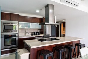 Eine moderne Küche mit Edelstahlgeräten, einer zentralen Kochinsel mit Sitzgelegenheiten und Holzschränken.