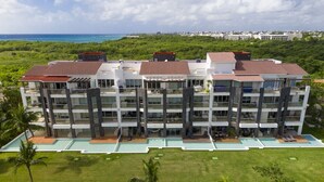 A multi-story hotel with a swimming pool, surrounded by greenery and a view of the ocean. - Mareazul, Playa del Carmen, Oceanfront Condo, Paraiso Azul (Playa del Carmen)