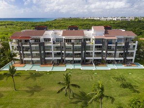 A multi-story hotel with a swimming pool, surrounded by greenery and a view of the ocean. - Mareazul, Playa del Carmen, Oceanfront Condo, Paraiso Azul (Playa del Carmen)