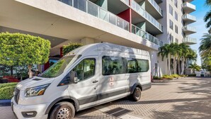 Een witte bus geparkeerd voor een modern gebouw met balkons en palmbomen.