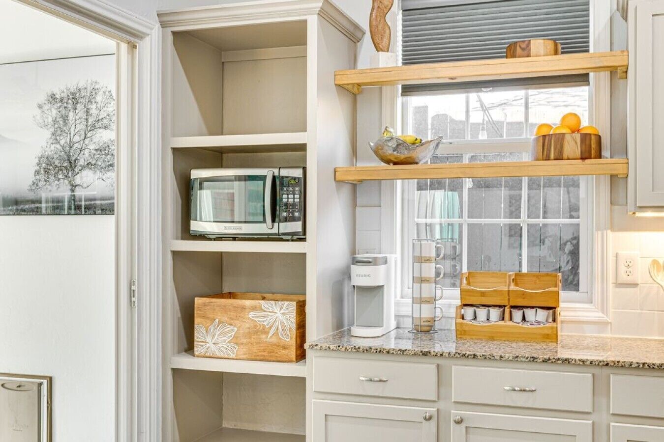 A kitchen with white cabinets, a microwave, a coffee maker, and a window with a view of trees.