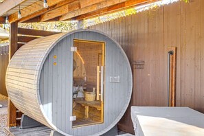 Un sauna avec une façade en bois et une porte en verre, situé à côté d’une structure également en bois.