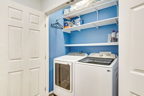 A laundry room with two white dryers, a blue wall, and shelves with laundry supplies. - Sauna, Hot Tub & Backyard Fun in OKC (Oklahoma City)