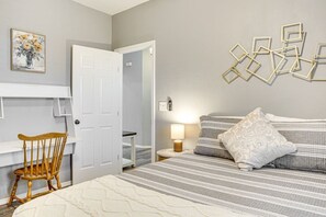 Ein Schlafzimmer mit einem Bett, einem Sessel, einem Nachttisch mit Lampe und einer Wand mit geometrischen Verzierungen.