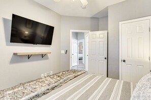 A bedroom with a flat-screen TV mounted on the wall, a patterned rug, and a door leading to another room. - Sauna, Hot Tub & Backyard Fun in OKC (Oklahoma City)