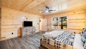 Une chambre avec un lit, une commode, un téléviseur et un ventilateur de plafond.