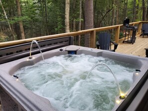 Un bain à remous sur une terrasse en bois, entouré d’arbres.