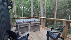 Une terrasse en bois avec un barbecue, deux chaises et une rambarde donnant sur une forêt.