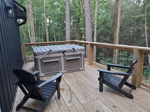 Eine Holzterrasse mit Grill, zwei Stühlen und einem Geländer, das auf einen Wald blickt.