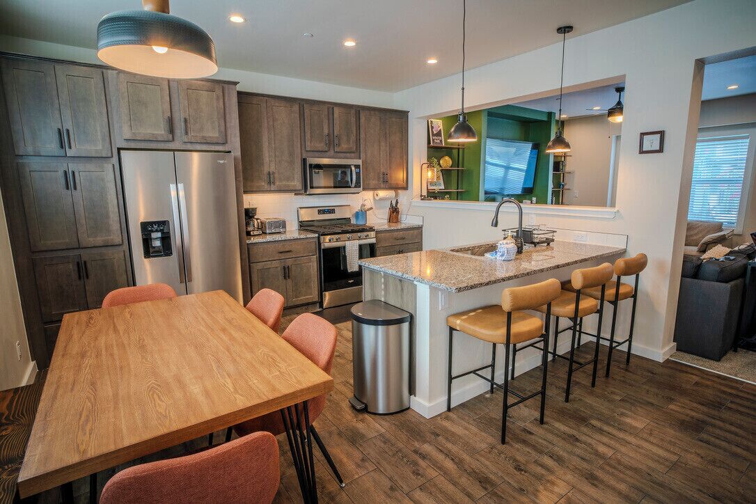 A modern kitchen with a central island, wooden cabinets, stainless steel appliances, and a dining area with a table and chairs.