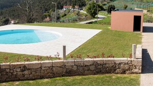Ein Pool mit Steinmauer, einer Rasenfläche und einem Gebäude im Hintergrund.