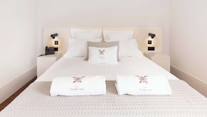 Ein ordentlich gemachtes Bett mit weißen Leinen, zwei Kissen mit einem Logo, Nachttischlampen und zwei Handtücher mit einem Logo.