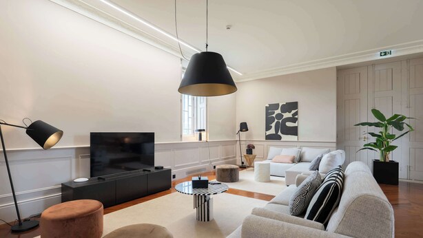 Ein modernes Wohnzimmer mit einer Couch, Hockern, einem Fernseher und einer Pendelleuchte.