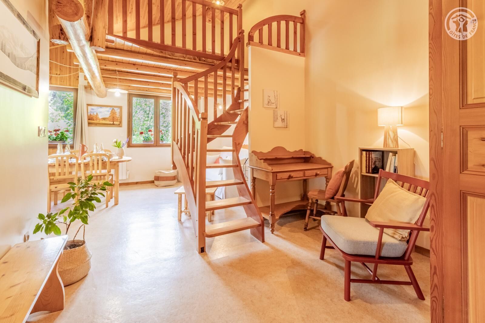 Un intérieur en bois avec un escalier en colimaçon, un coin repas avec des meubles en bois et un bureau avec une chaise.