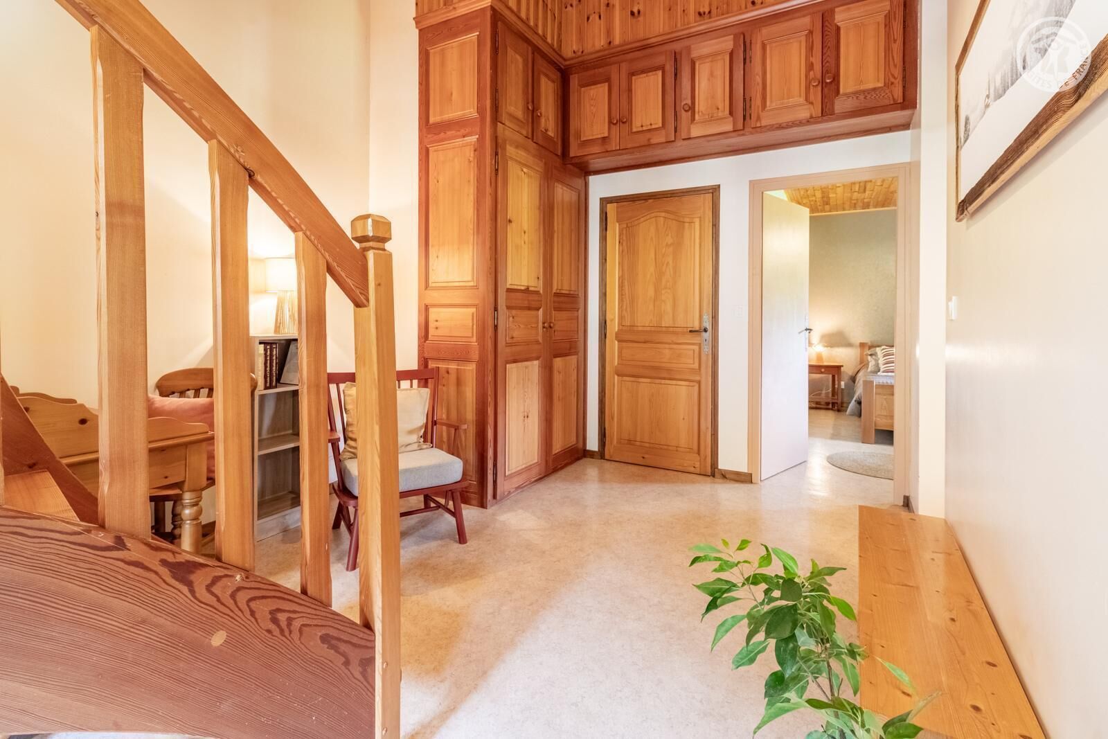 A wooden staircase leading to a bedroom with a bed, a chair, and a plant.