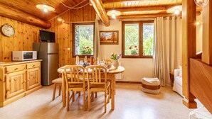 A wooden cabin interior with a dining table, chairs, a kitchen area with appliances, and a large window with curtains. - Androsace - VAL CENIS (VAL CENIS)