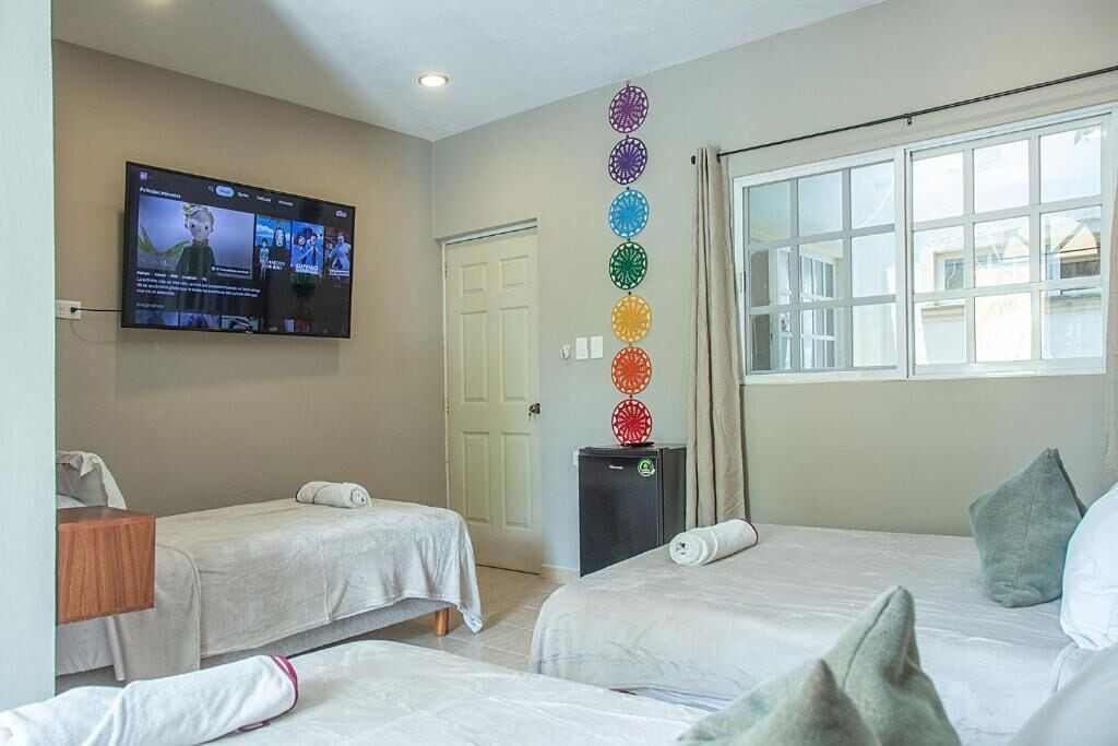 A hotel room with two beds, a television mounted on the wall, a door, and a window with curtains.