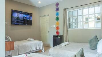 A hotel room with two beds, a television mounted on the wall, a door, and a window with curtains.