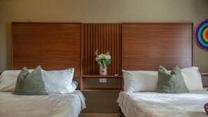 A hotel room with two beds, a wooden headboard, a nightstand with a vase of flowers, and a colorful circular wall decoration.