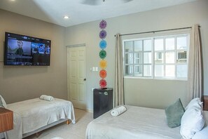 A hotel room with two beds, a television mounted on the wall, a window with curtains, and a decorative wall hanging. - Villas Aura (Merida)