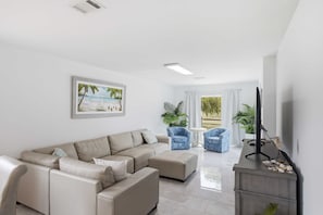 A modern living room with a beige sectional sofa, two blue armchairs, a small white table, and a TV on a grey stand. - New- Eastpoint- Next to RV park (Eastpoint)