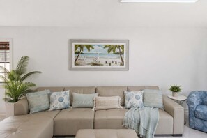 A beige sofa with multiple cushions, a framed beach scene painting, and a potted plant. - New- Eastpoint- Next to RV park- Pet Friendly (Eastpoint)