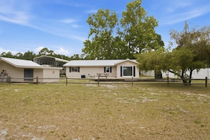 A mobile home with a covered porch, a fenced yard, and a large tree in the background. - New- Eastpoint- Next to RV park (Eastpoint)