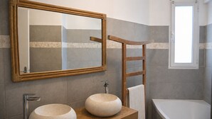 Un baño con un espejo de marco de madera, dos lavamanos redondos, un perchero para toallas y una ventana.