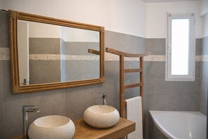 Ein Badezimmer mit einem spiegel, der in einem Holzrahmen gefasst ist, zwei runden Waschbecken, einem Handtuchhalter und einem Fenster.