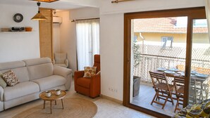 Una sala de estar con sofá, sillón y mesa de centro, un comedor con mesa y sillas, y un ventanal corredizo que da a un patio exterior.