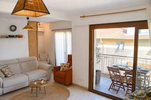 Ein Wohnzimmer mit Sofa, Sessel und Couchtisch, ein Essbereich mit Tisch und Stühlen sowie eine Glasschiebetür, die auf eine Terrasse im Freien führt.