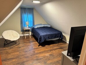 A small, triangular attic bedroom with a bed, a chair, and a television.