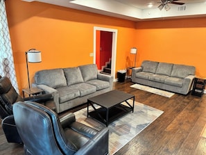 A living room with two grey sofas, a black coffee table, and a black leather chair. - Spacious Jonesboro Retreat | Near Downtown | Fully Stocked Kitchen | Smart TVs (Jonesboro)