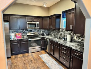 A modern kitchen with dark cabinetry, stainless steel appliances, and a patterned backsplash. - Spacious Jonesboro Retreat | Near Downtown | Fully Stocked Kitchen | Smart TVs (Jonesboro)