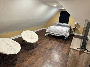 A bedroom with a bed, two chairs, a TV, and a ceiling fan. - Spacious Jonesboro Retreat | Near Downtown | Fully Stocked Kitchen | Smart TVs (Jonesboro)