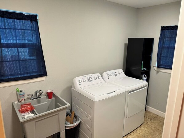 A laundry room with two washing machines, a sink, and a small trash bin.