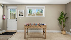 A room with a foosball table, a door, a window, and a potted plant. - Family Basement Retreat Near Rockies (Okotoks)