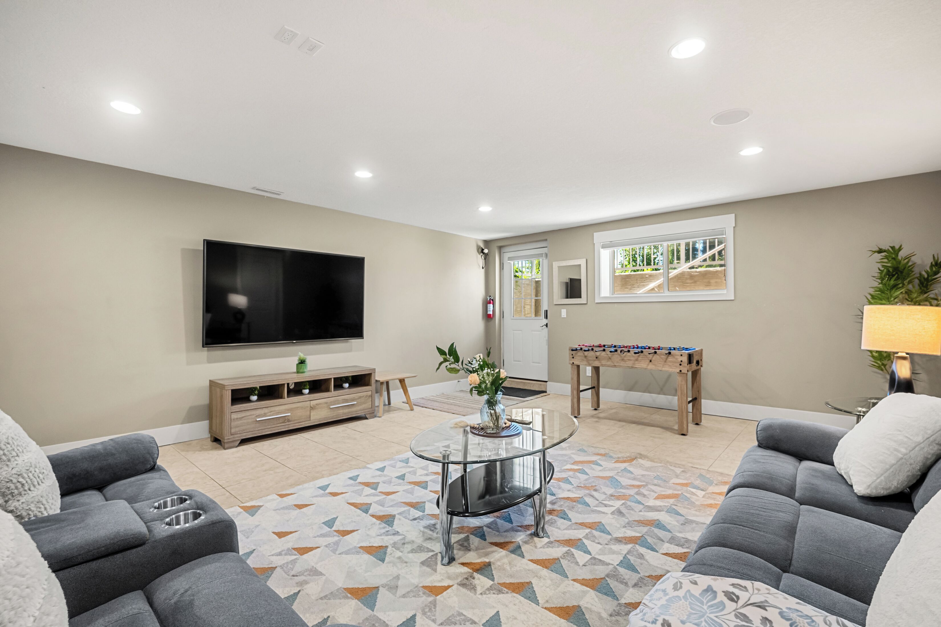 A living room with a flat-screen TV, sofa, coffee table, and a foosball table.