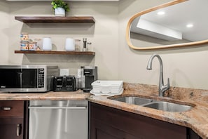 Una cocina moderna con lavavajillas incorporado, microondas, tostadora, cafetera y un lavabo con grifo moderno.